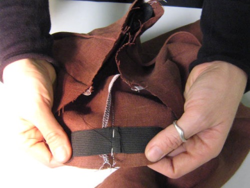 A pair of hands sews elastic into a waistband.